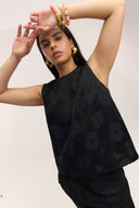 Woman wearing a black sleeveless top with floral patterns against a plain background