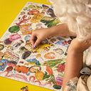 Person assembling a colorful puzzle with various illustrations on a yellow surface