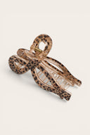 A leopard print hair claw clip with a metallic rose gold-toned inner frame, shown on a light cream background.