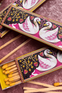 Matches with decorative packaging featuring swan designs on a textured surface.