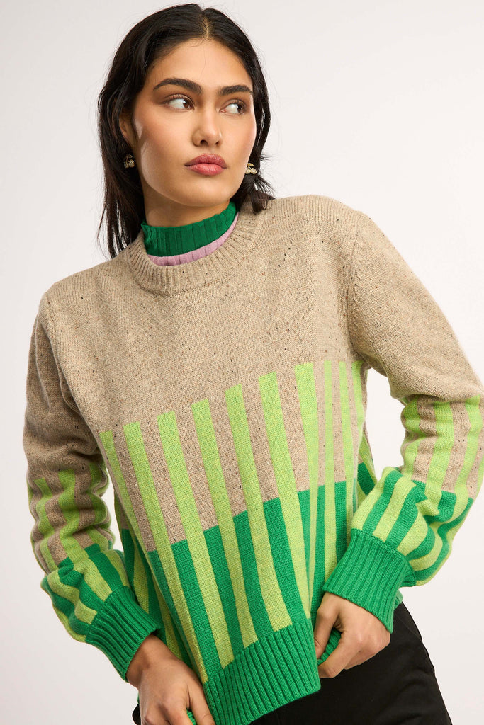 Person wearing a beige sweater with green and light green striped patterns on a plain background