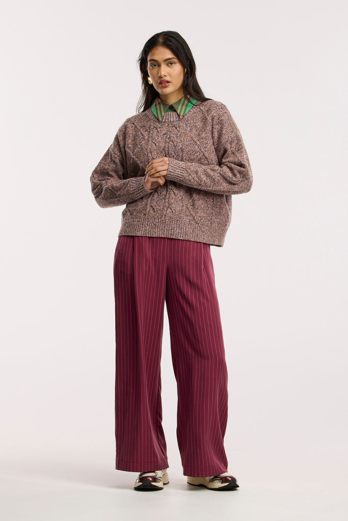 Woman wearing a cable knit sweater and maroon pants on a white background