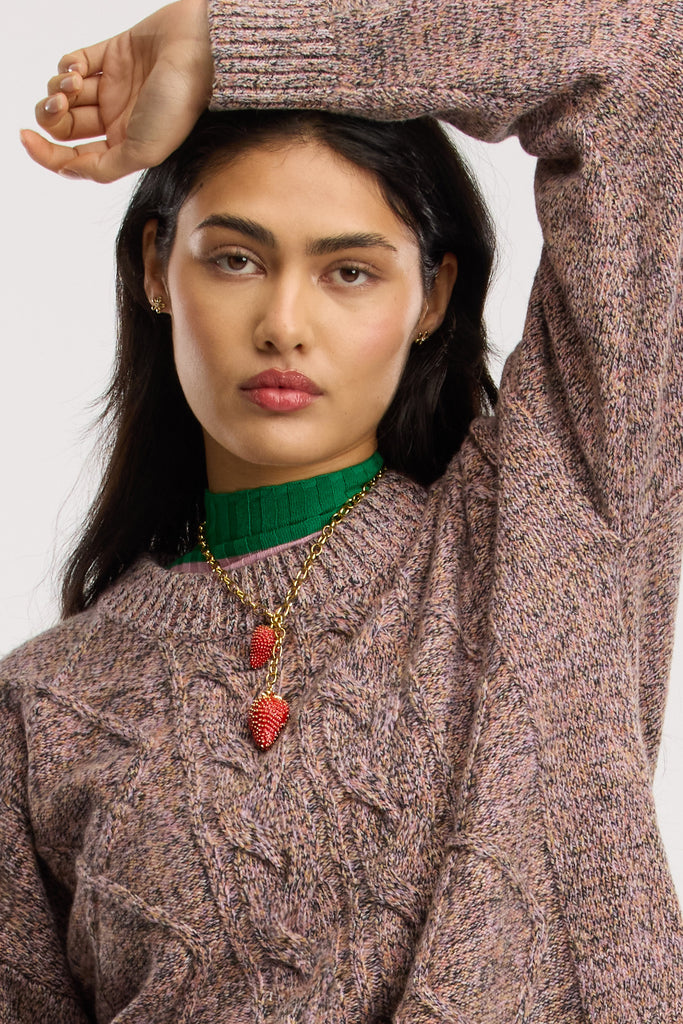 Woman wearing a cable knit sweater with a red strawberry pendant necklace against a white background
