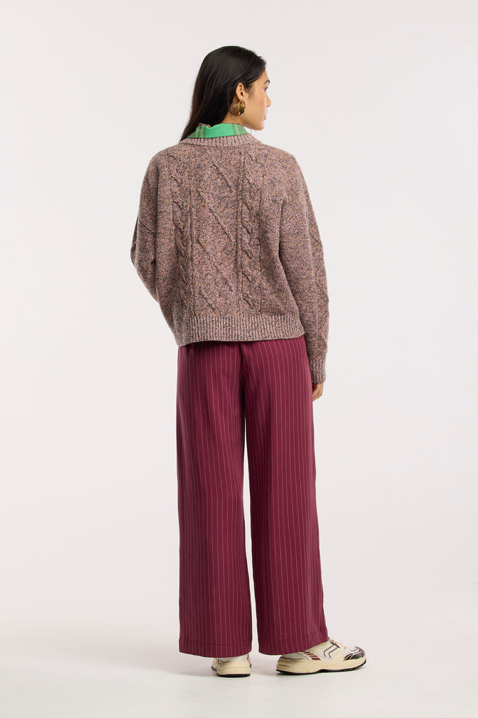 Person wearing a cable knit sweater and burgundy pants on a white background