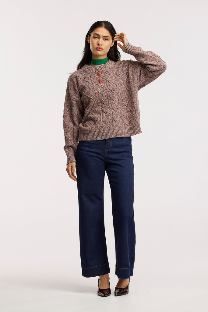 Woman wearing a cable knit sweater and blue jeans on a white background