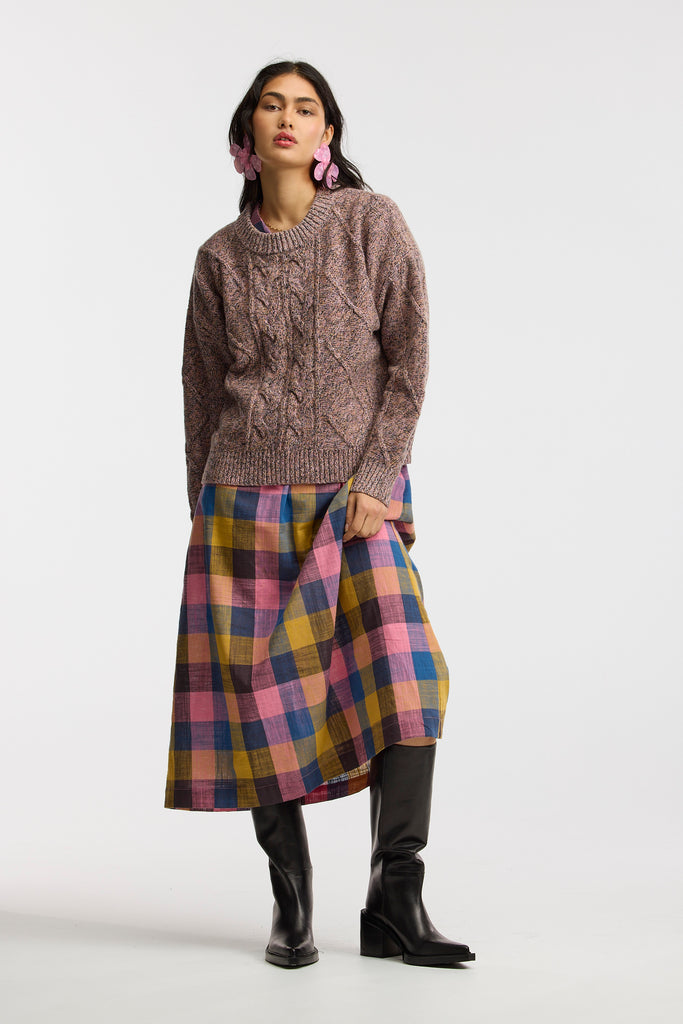 Woman wearing a cable knit sweater and plaid skirt on a white background