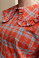 Close-up of a person wearing a bright orange and light blue plaid blouse with a ruffled Peter Pan collar and button front.